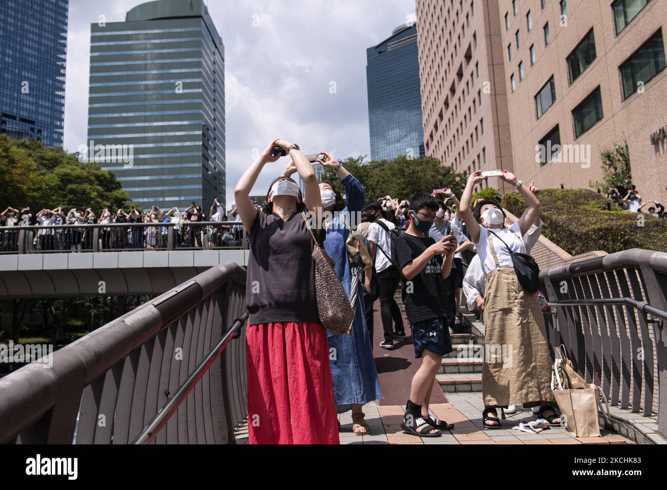Le persone puntano i loro cellulari verso il cielo per scattare una foto lo squadrone acrobatico Blue Impulse dell'Air Self-Defense forceÂ che disegna gli anelli olimpici su Tokyo, Giappone, il 23 luglio 2021. (Foto di Yusuke Harada/NurPhoto) Foto Stock