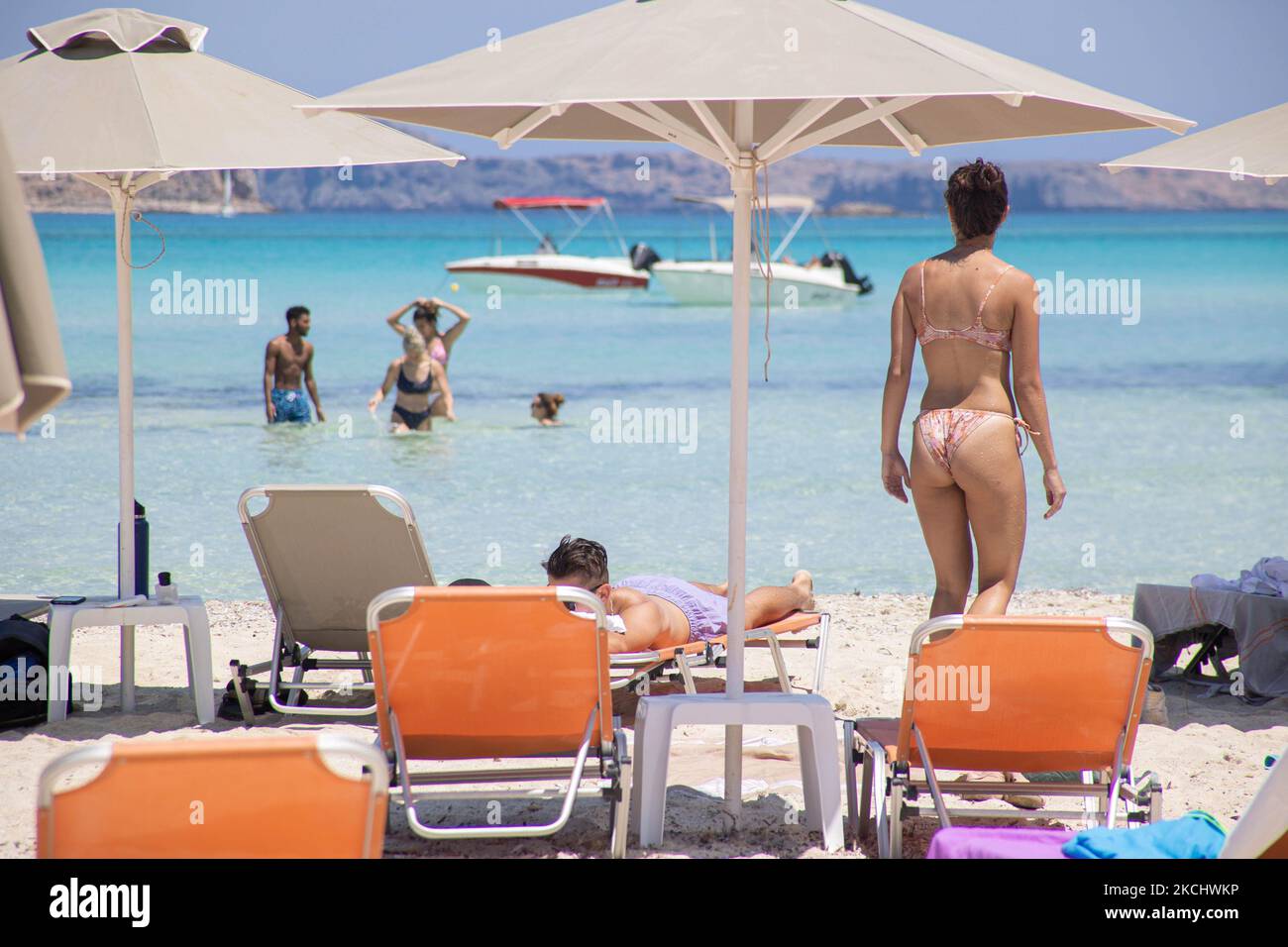 Persone, uomini e donne con bikini e costume da bagno godono l'acqua di Balos Beach o l'ombra sotto un ombrello del bar sulla spiaggia locale presso l'incredibile laguna, con la piscina come le acque turchesi esotiche e tropicali del mare Mediterraneo si trova nella regione di Chania, nell'isola di Creta. Balos è una delle spiagge più visitate di Creta e popolare per i visitatori di tutto il mondo. Acque cristalline, la laguna, montagne rocciose ripide, un bar sulla spiaggia che fornisce ombrelloni e ombra con bevande e un'isola pirata si trovano nella stessa regione che è accessibile da un trekking di 20 minuti o in barca. La Grecia è alla prova Foto Stock