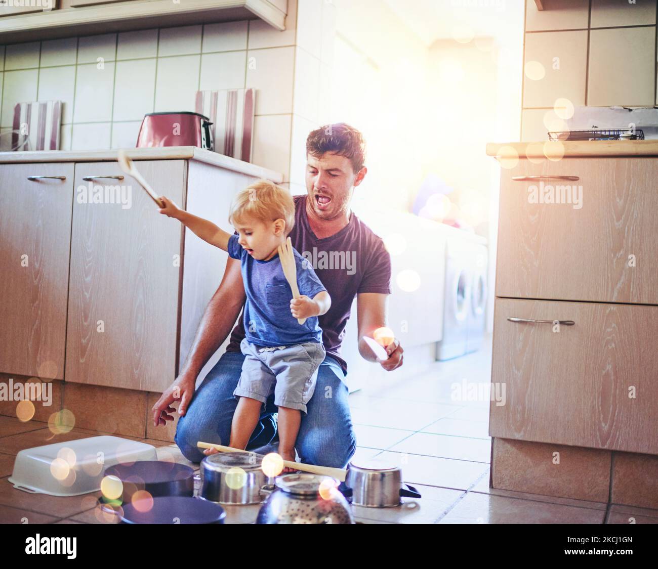 È nato per il rock, un padre che guarda il suo figlio mentre suona la batteria sulle pentole del pavimento della cucina. Foto Stock