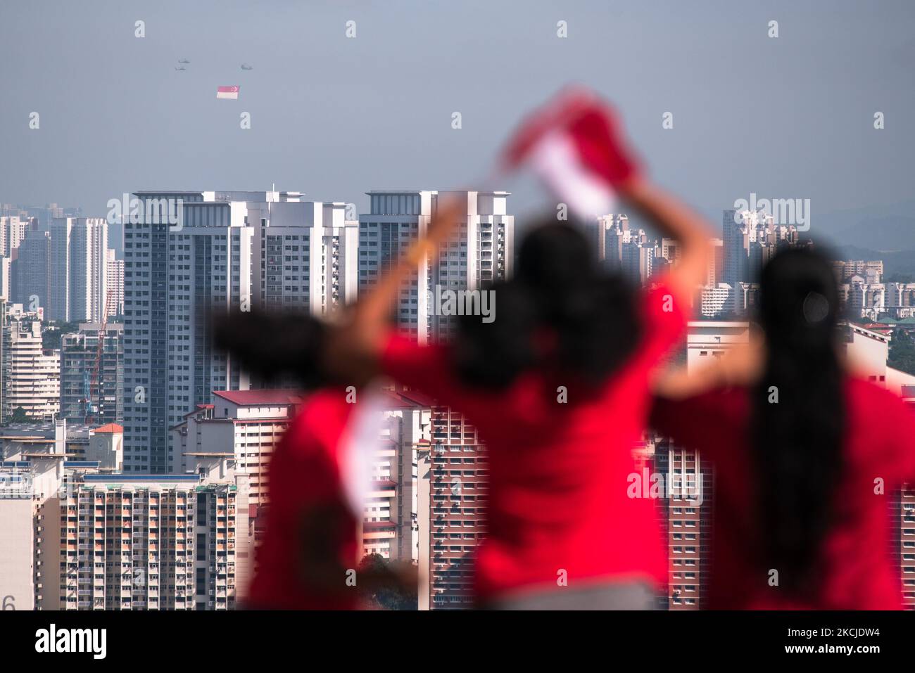 Gli spettatori salutano gli elicotteri militari con la bandiera di Singapore in lontananza mentre la nazione celebra il 56th° anniversario della sua indipendenza lunedì 9 agosto 2021 a Singapore. La tradizionale sfilata e spettacolo sono stati silenziati dopo un'epidemia di luglio, le misure di sicurezza pandemiche saranno allentate domani, 10 agosto, per consentire la cena e l'esercizio al chiuso in gruppi per le persone vacinate. (Foto di Joseph Nair/NurPhoto) Foto Stock