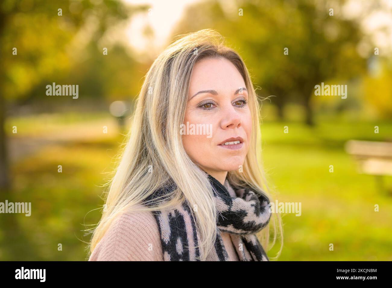 Ritratto di una donna penosa di mezza età che indossa un maglione e una sciarpa in un parco in autunno Foto Stock