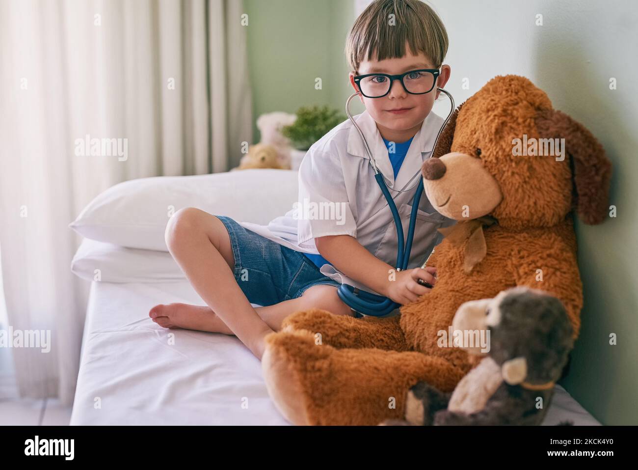 Questo potrebbe portare ad una carriera in medicina: Un ragazzino che finge di essere un medico mentre esamina il suo orsacchiotto. Foto Stock