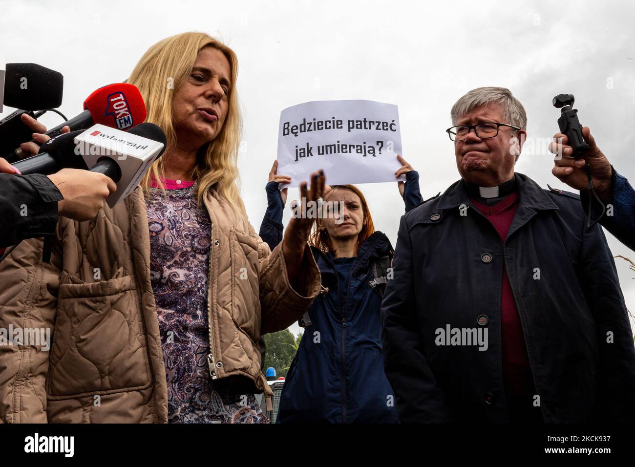 Gli attivisti protestano mentre i soldati dell'esercito polacco circondano un gruppo di immigrati dall'Afghanistan al confine bielorusso e impediscono il loro ingresso nel paese di Usnarz Gorny, Polonia, il 27 agosto 2021. L'esercito e la polizia hanno fermato i migranti al confine e hanno impedito loro di andare in Polonia, l'esercito ha anche rifiutato l'accesso alle procedure di asilo, assistenza medica e cibo. Giornalisti e operatori di beneficenza sono tenuti a circa 300 metri di distanza. Le azioni del governo polacco sono state ampiamente criticate. Il governo polacco ha anche deciso di costruire una recinzione per fermare un afflusso di migranti che camminano Foto Stock