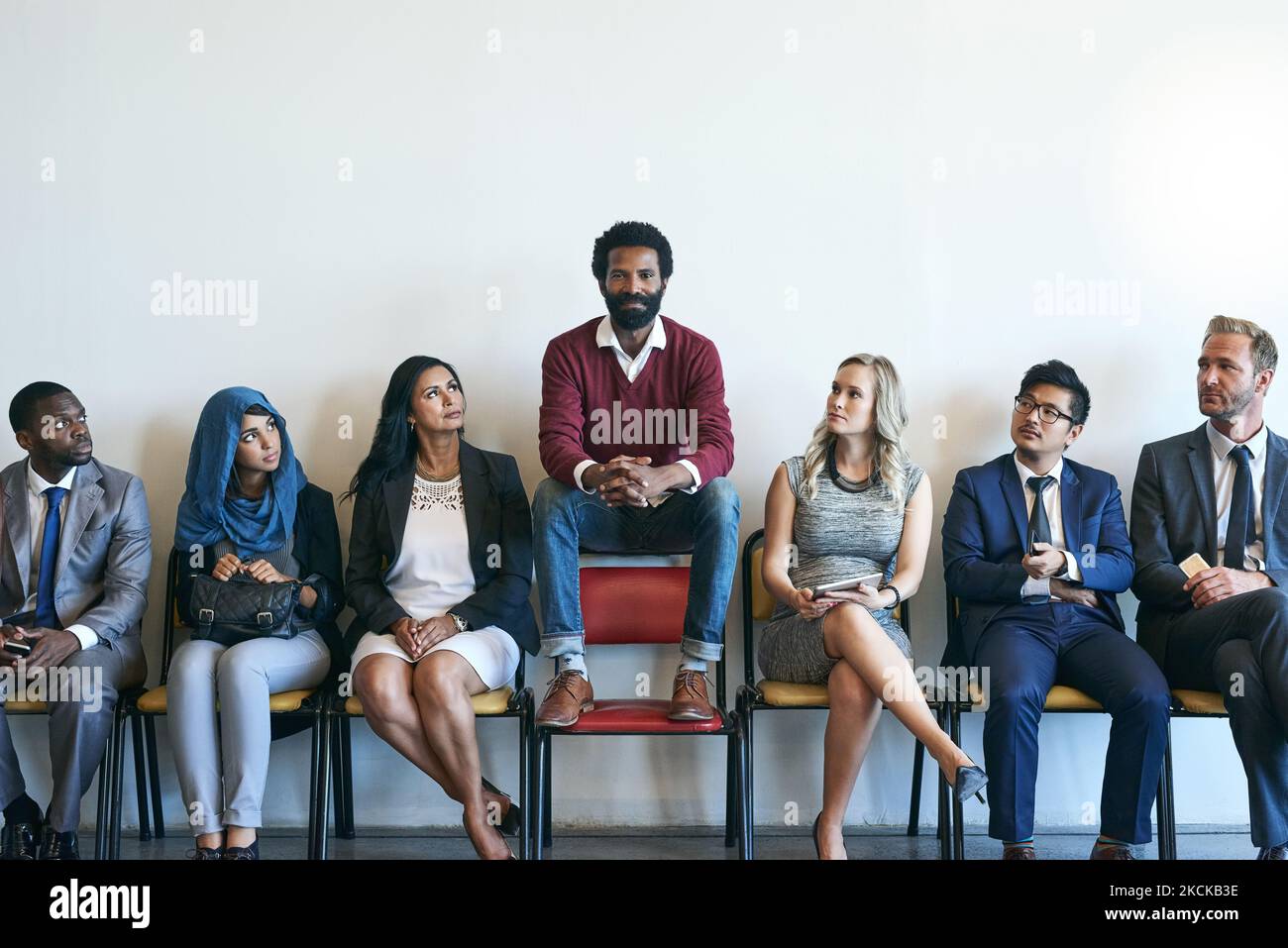 Distinguersi dalla folla. Ritratto di un candidato felice di lavoro seduto in fila con un gruppo di uomini d'affari ben vestiti. Foto Stock