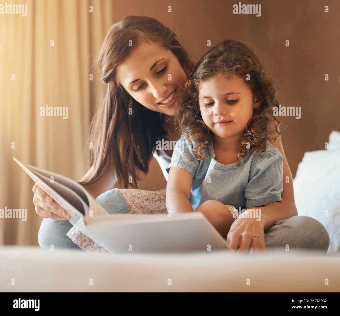 Possiamo vivere in un castello un giorno. Una madre felice e una figlia a casa a leggere un libro di storia sul letto. Foto Stock