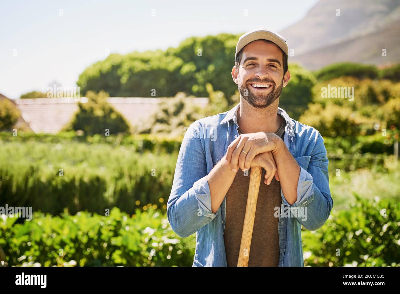 La mia fattoria è la mia vita. Ritratto di un giovane agricoltore felice che tiene una spade mentre si posa nei campi della sua fattoria. Foto Stock