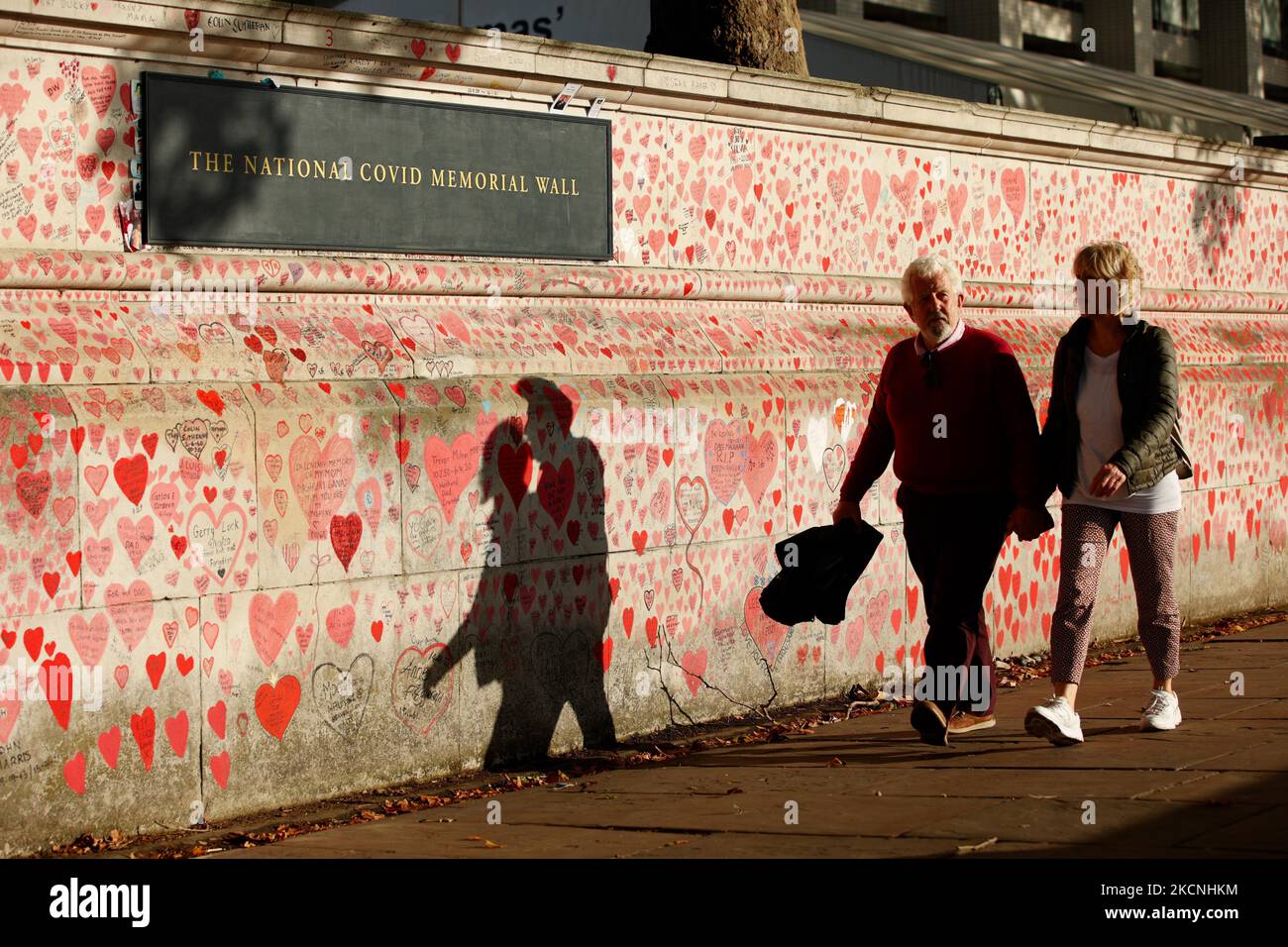 Una coppia cammina accanto al National Covid Memorial Wall sulla sponda sud del Tamigi, di fronte alle Houses of Parliament a Londra, Inghilterra, il 27 settembre 2021. Il muro, creato questa primavera, è costituito da più di 150.000 cuori dipinti, ciascuno che rappresenta una vita persa nel paese per covid-19. (Foto di David Cliff/NurPhoto) Foto Stock