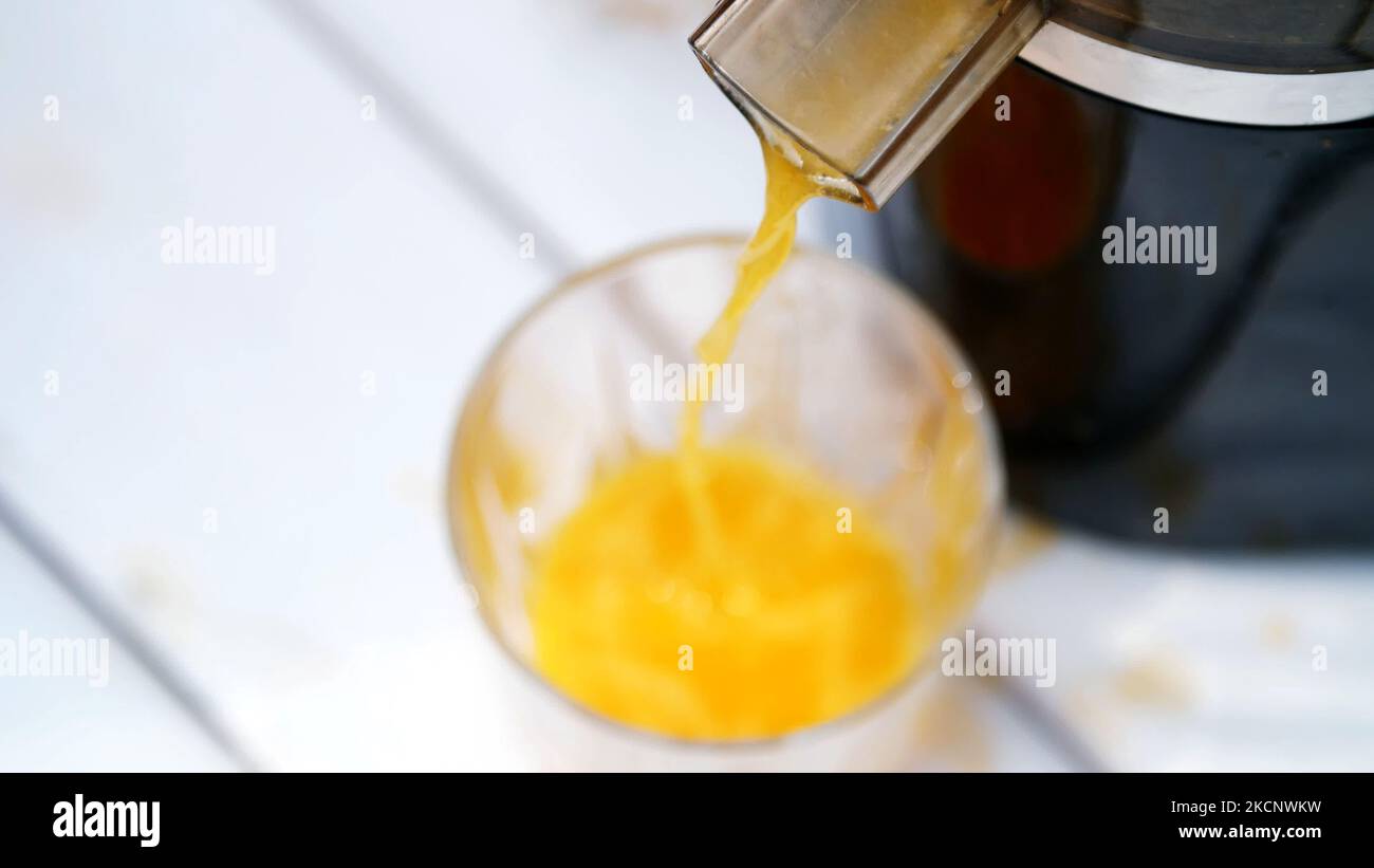 in primo piano, dalla centrifuga scorre il succo d'arancia appena spremuto in un bicchiere. vista dall'alto. Foto di alta qualità Foto Stock
