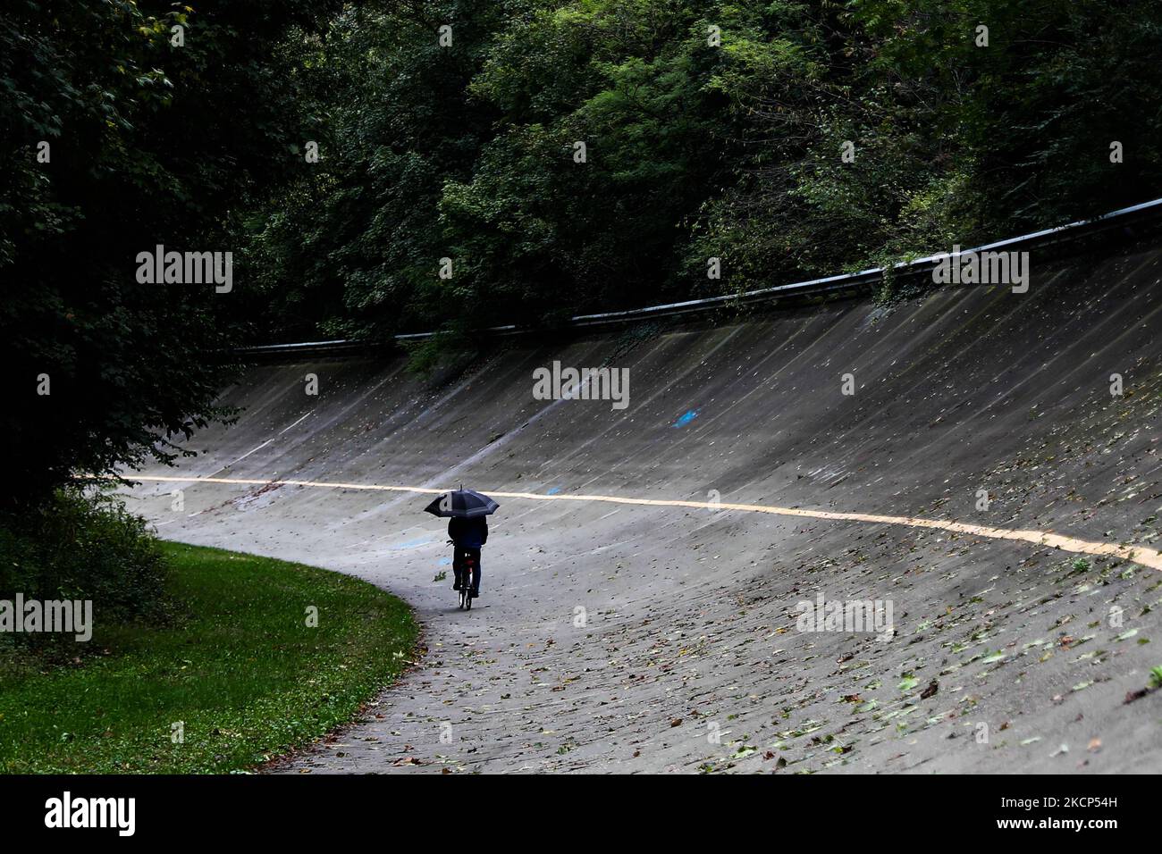 Un uomo con un ombrello si sposta in bicicletta sulla vecchia sezione ovale del circuito di Monza il 5 ottobre 2021. (Foto di Jakub Porzycki/NurPhoto) Foto Stock