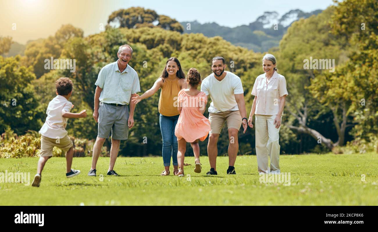 Grande famiglia, parco naturale e felice di giocare con i bambini che corrono sull'erba con i nonni anziani, mamma e papà sorridono nel sole estivo. Madre divertente Foto Stock