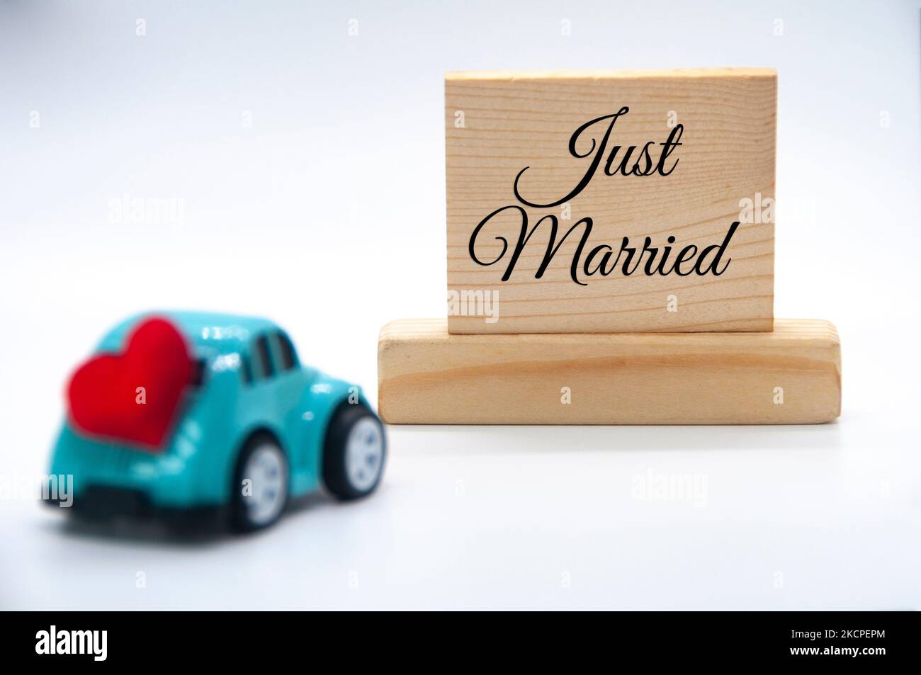 Mini macchina giocattolo con forma a cuore rosso con testo appena sposato su sfondo blocchi di legno. Concetto di matrimonio. Foto Stock