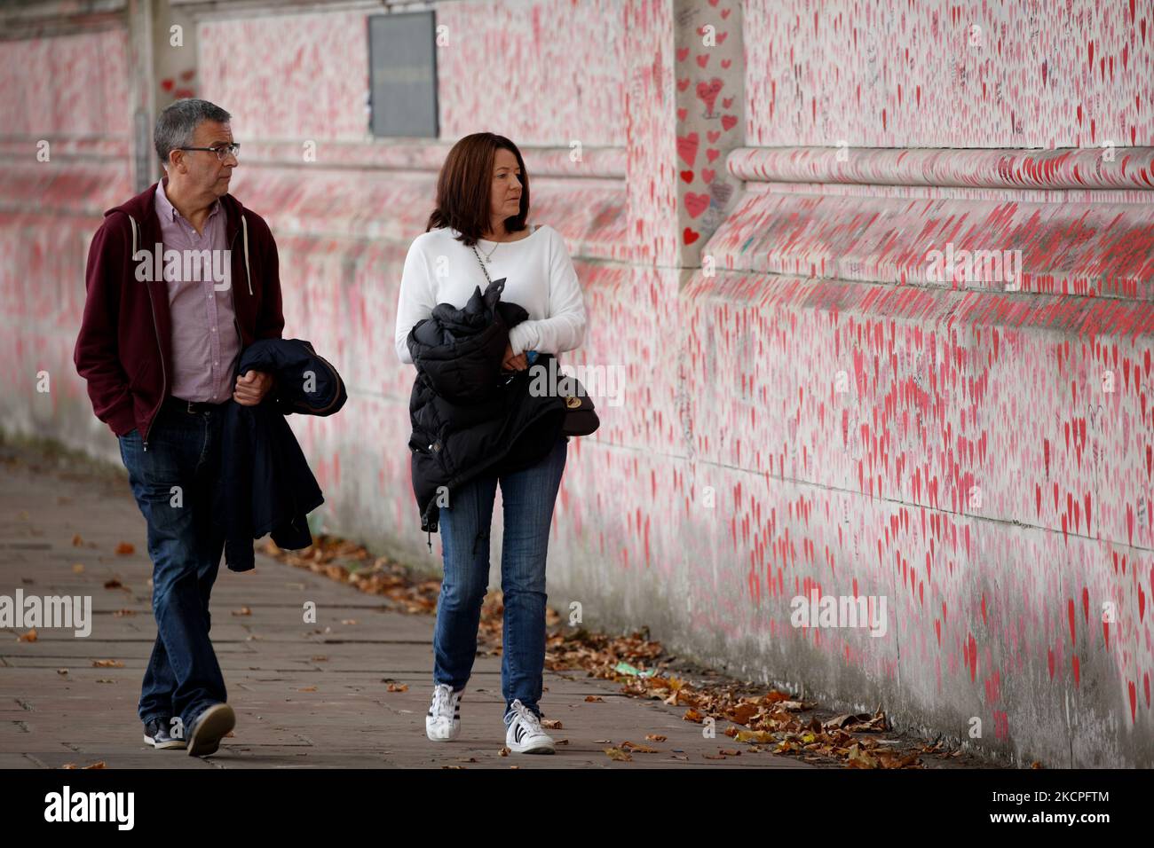 Un uomo e una donna guardano il National Covid Memorial Wall sulla sponda sud del Tamigi, di fronte alle Houses of Parliament a Londra, in Inghilterra, il 12 ottobre 2021. Il muro, creato questa primavera, è costituito da più di 150.000 cuori dipinti, ciascuno che rappresenta una vita persa nel paese per covid-19. Oggi nel frattempo è stata pubblicata la relazione "Coronavirus: Lezioni apprese fino ad oggi" dei parlamentari sui comitati per la salute e l'assistenza sociale e la scienza e la tecnologia, che critica fortemente l'approccio del governo alla gestione delle prime fasi della pandemia di coronavirus, ma anche Foto Stock