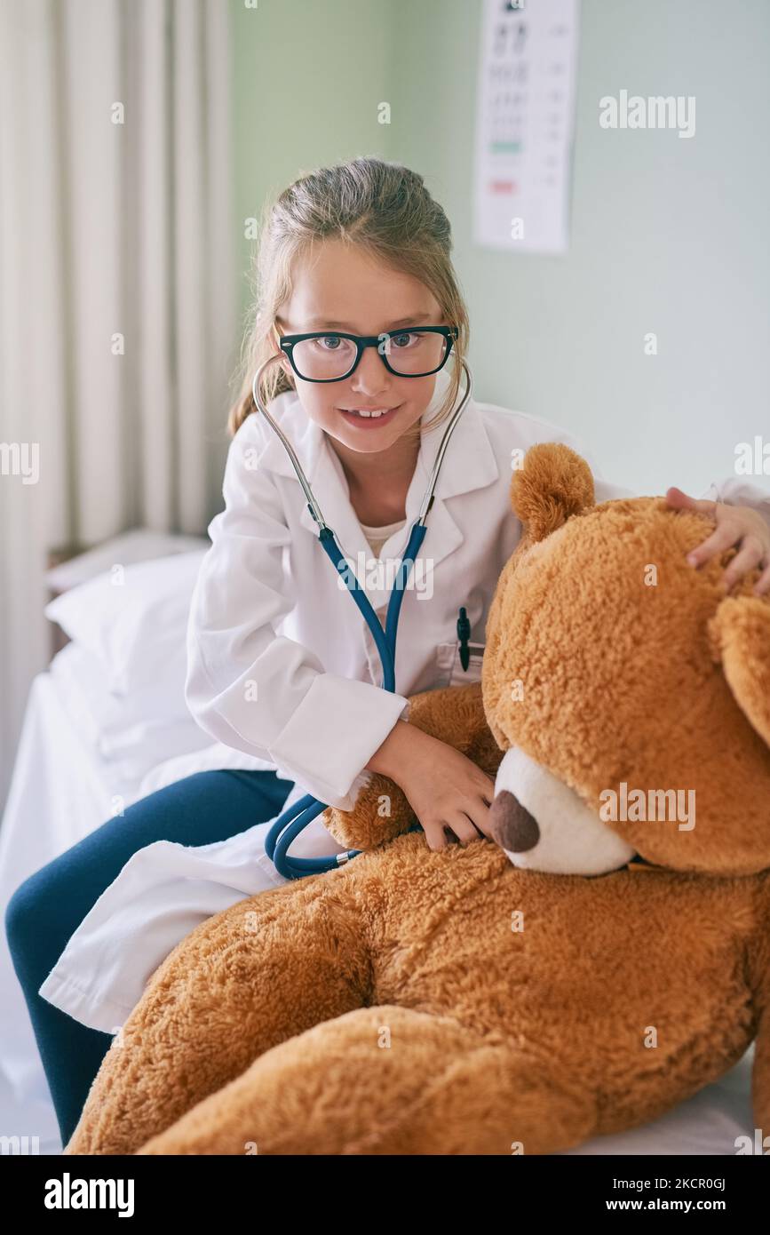 Imparando la medicina da una giovane età. Una bambina che finge di essere un medico mentre esamina il suo orsacchiotto. Foto Stock