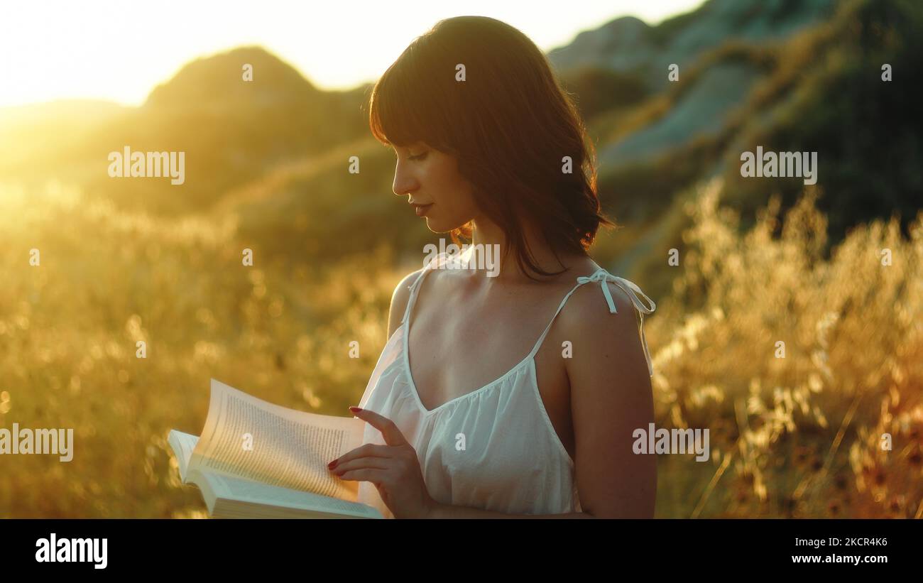 Donna che legge un libro all'aperto al tramonto Foto Stock