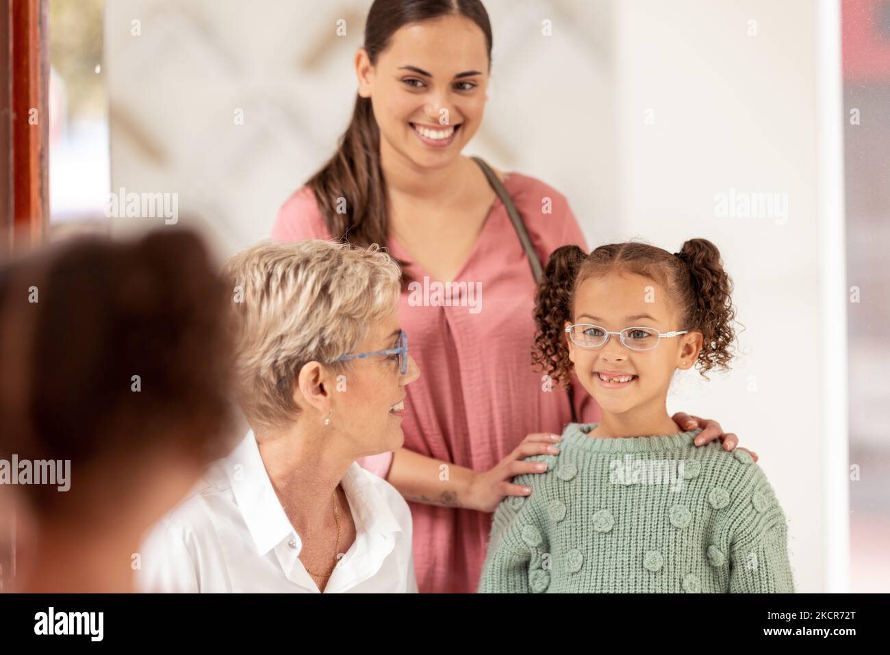 Specchio, visione e ragazza che provano sugli occhiali in un negozio ottico con la sua madre e l'optometrista senior. Felice, sorridere e bambino scegliendo una cornice per gli occhiali Foto Stock