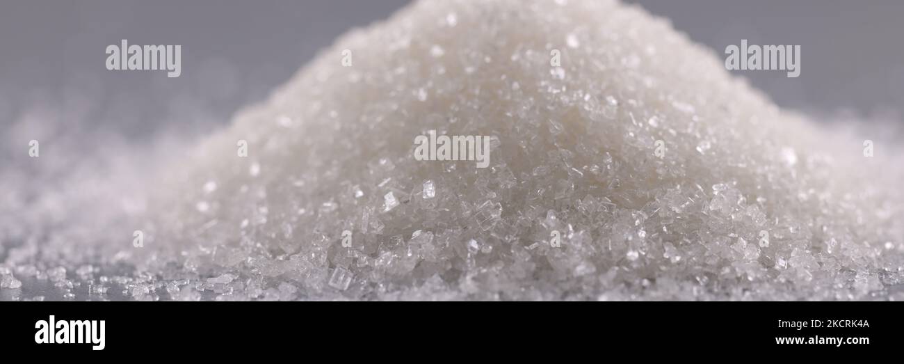 Mucchio di cristalli di zucchero sulla superficie grigia, mucchio di polvere dolce da aggiungere in piatti Foto Stock