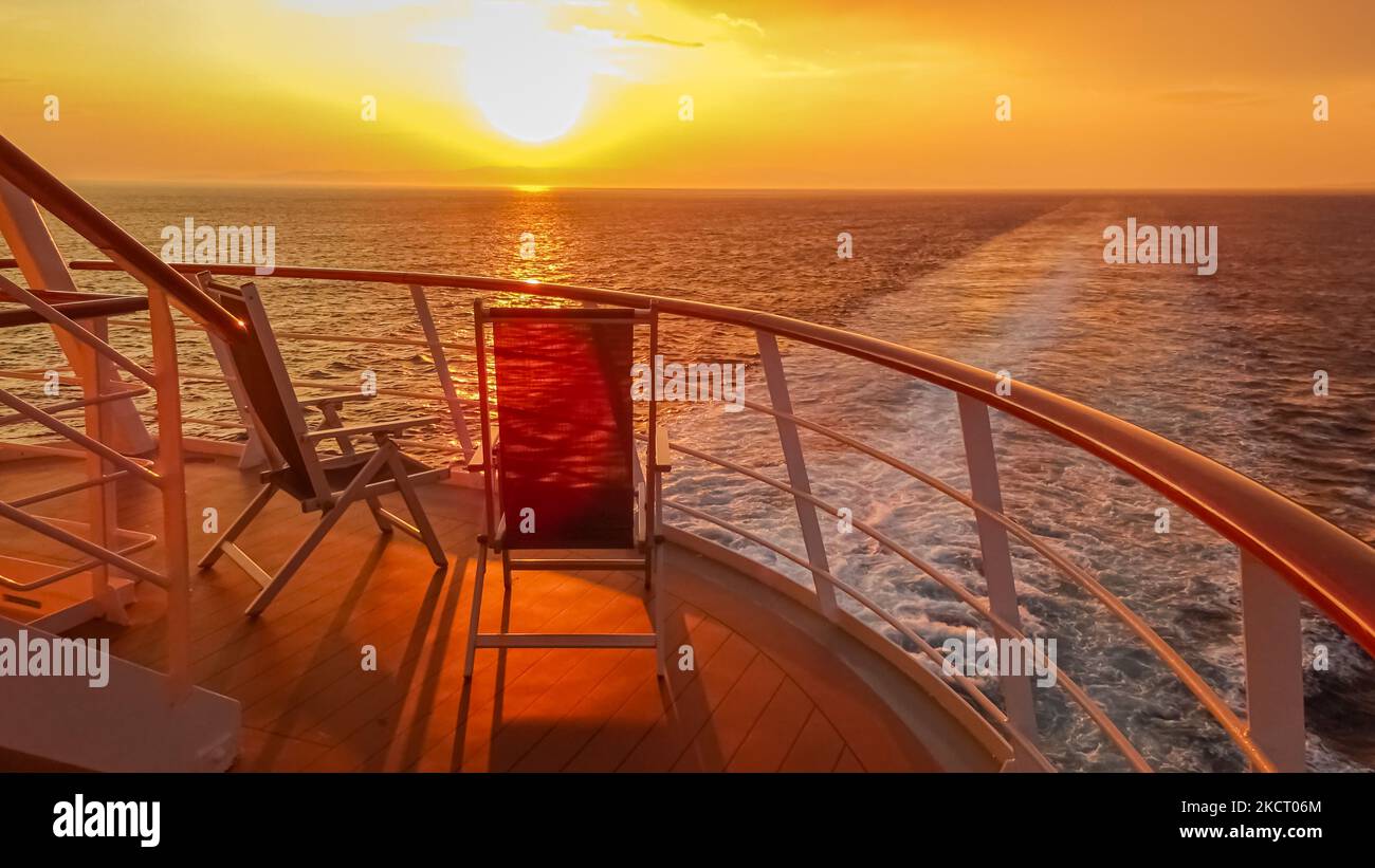 Vista di due sedie a sdraio sul ponte di una nave da crociera al tramonto sulla scia della nave da crociera. Vista dalla poppa della nave. Foto Stock