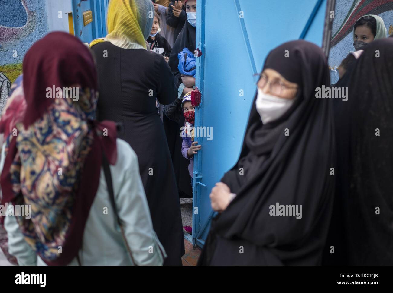 Una studentessa afghana che indossa una maschera protettiva guarda come le madri afghane di scolaresche e scolari rifugiati aspettano i loro figli mentre si trovano alla porta della scuola di Farhang nel primo giorno del nuovo anno accademico? Nel sud di Teheran il 1 novembre 2021. La scuola di Farhang è stata fondata nel 2000 dal rifugiato afgano Nader Mousavi che si è laureato in sociologia presso l'Università di Teheran, per i bambini rifugiati afghani, E ora due anni dopo l'inizio dell'epidemia COVID-19 in Iran, dove la scuola era in funzione a tempo parziale, ha iniziato a funzionare a tempo pieno e. Foto Stock