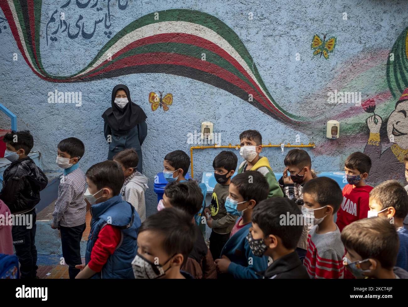 Insegnante afghana di sesso femminile, Fatemeh Hosseini che è venuta in Iran quando era un bambino di sette anni (Top) che indossa una maschera protettiva come scolari rifugiati line-up presso la scuola di Fahang nel primo giorno del nuovo anno accademico? Nel sud di Teheran il 1 novembre 2021. La scuola di Farhang è stata fondata nel 2000 dal rifugiato afgano Nader Mousavi che si è laureato in sociologia presso l'Università di Teheran, per i bambini rifugiati afghani, E ora, due anni dopo l'inizio dell'epidemia COVID-19 in Iran, dove la scuola operava a tempo parziale, ha iniziato ad operare a tempo pieno e afghana Foto Stock