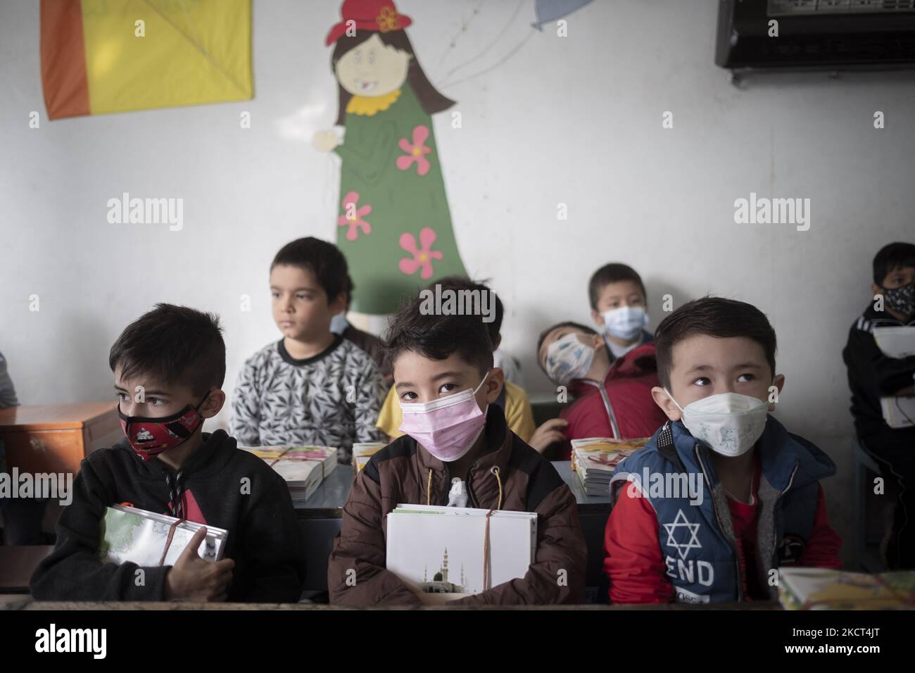 Gli scolari afghani rifugiati che indossano maschere protettive guardano su come tiene i loro libri mentre si siedono in un'aula alla scuola di Farhang nel primo giorno del nuovo anno accademico? Nel sud di Teheran il 1 novembre 2021. La scuola di Farhang è stata fondata nel 2000 dal rifugiato afgano Nader Mousavi che si è laureato in sociologia presso l'Università di Teheran, per i bambini rifugiati afghani, E ora due anni dopo l’inizio dell’epidemia COVID-19 in Iran, dove la scuola operava a tempo parziale, ha iniziato ad operare a tempo pieno e le scolaresche e gli scolari afghani possono attere Foto Stock