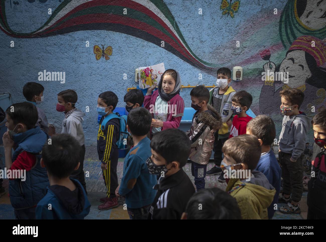 Una studentessa afghana rifugiata porta con sé i suoi libri scolastici come studenti rifugiati che si allineano per ricevere libri scolastici alla scuola di Farhang nel primo giorno del nuovo anno accademico? Nel sud di Teheran il 1 novembre 2021. La scuola di Farhang è stata fondata nel 2000 dal rifugiato afgano Nader Mousavi che si è laureato in sociologia presso l'Università di Teheran, per i bambini rifugiati afghani, E ora due anni dopo l’inizio dell’epidemia COVID-19 in Iran, dove la scuola operava a tempo parziale, ha iniziato a funzionare a tempo pieno e le scolaresche e gli scolari afghani possono frequentare la scuola. F Foto Stock