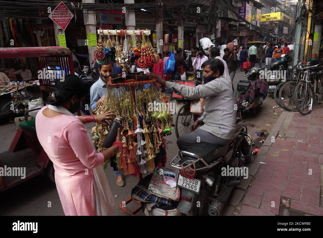 Un fornitore siede su una bici mentre i clienti passano attraverso gli articoli in un mercato a Nuova Delhi, India il 24 novembre 2021. La Reserve Bank of India prevede una crescita del PIL del 9,5 per cento quest'anno fiscale, mentre la proiezione media varia tra il 8,5 per cento e il 10 per cento, rispetto alla precedente stima del 8 per cento per l'anno civile 2022. (Foto di Mayank Makhija/NurPhoto) Foto Stock