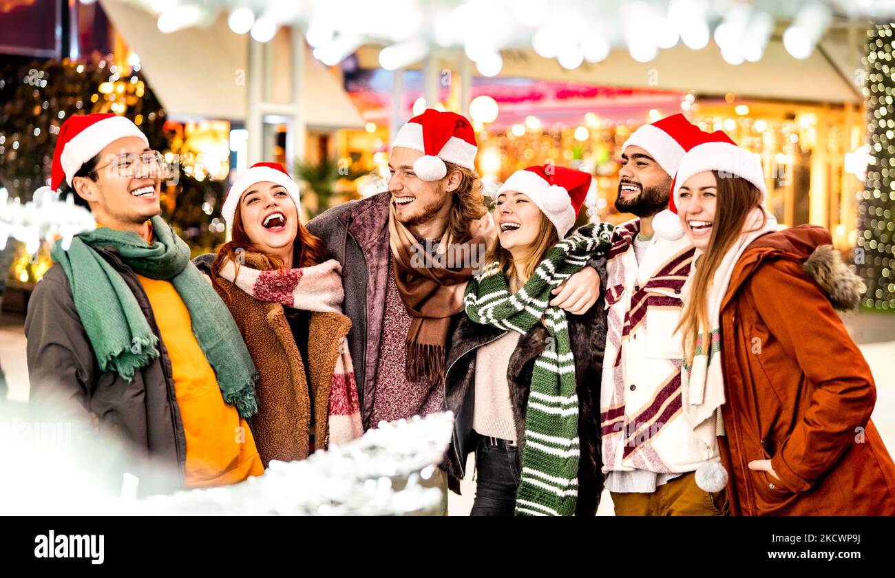 Felice gruppo di amici a piedi in città durante le vacanze di Natale - concetto di stile di vita invernale con giovani multiculturali che indossano cappelli di santa rosso che hanno fu Foto Stock