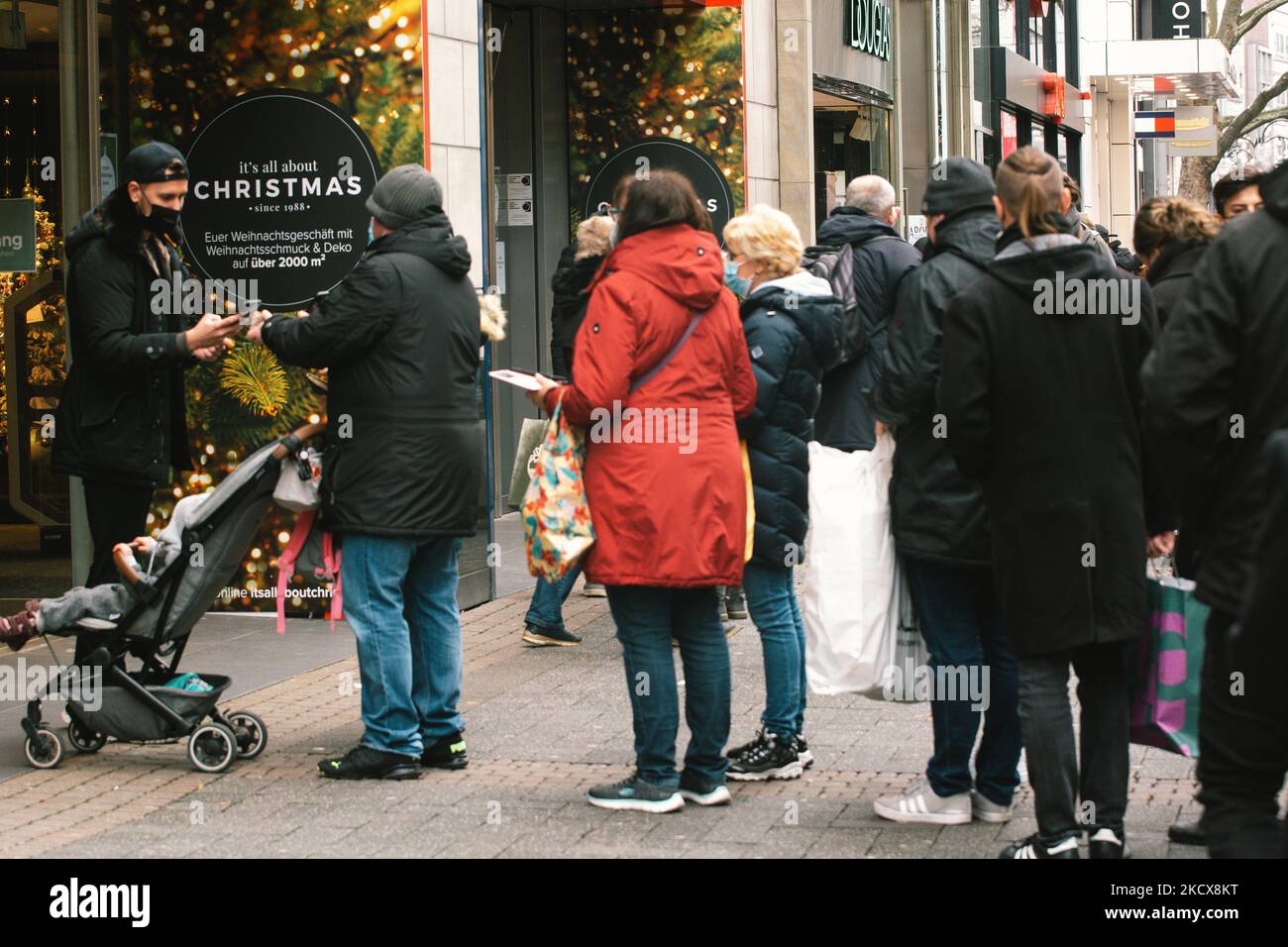 Le persone aspettano in coda per mostrare la prova digitale del vaccino per entrare in deposito nel centro di colonia, in Germania, il 4 dicembre 2021, dal momento che la Germania inizia ad escludere i non vaccinati da una certa vita sociale. (Foto di Ying Tang/NurPhoto) Foto Stock