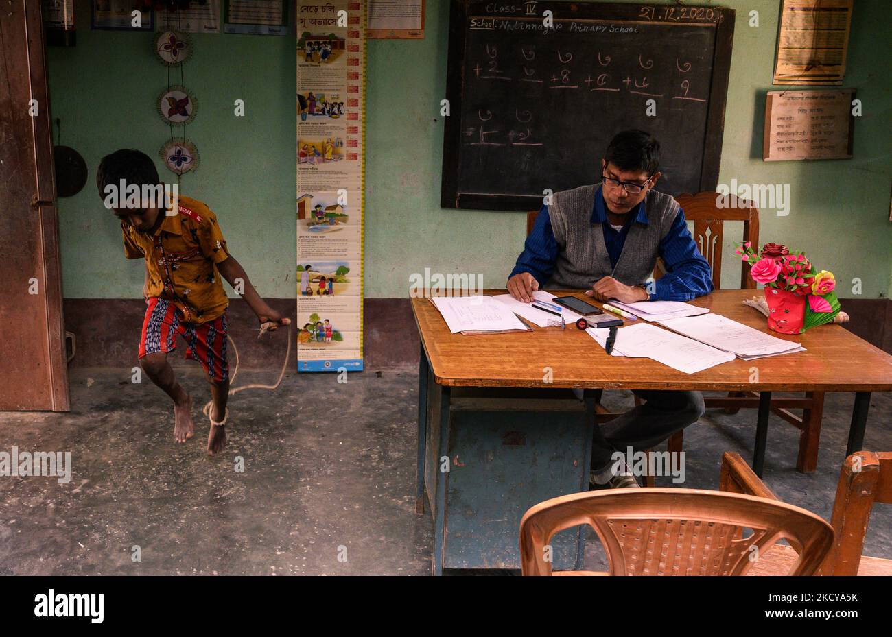 Il capomastro sta facendo un foglio del contrassegno e gli allievi giocano con la corda di salto ed entrano ripetutamente nella stanza dell'ufficio ad una scuola primaria rurale a Nabin Nagar, Bengala occidentale, India il 21/12/2021. (Foto di Soumyabrata Roy/NurPhoto) Foto Stock