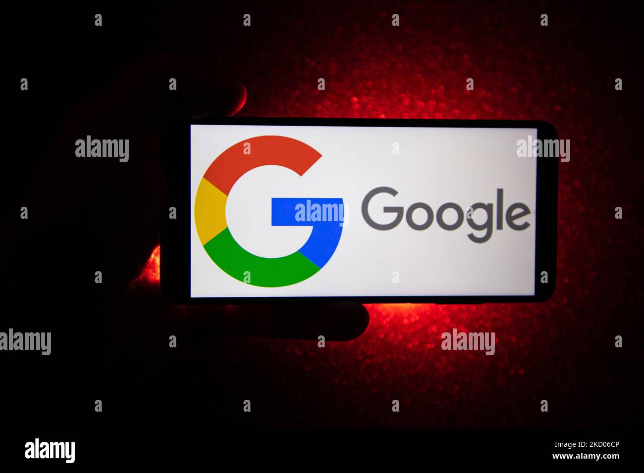 Logo Google su uno smartphone tenuto da una mano con sfondo rosso scuro. Logo Google closeup visualizzato su uno schermo del telefono, smartphone il logo o il motore di ricerca in vari sfondi come la tastiera, la texture illuminata scura o uno schermo del computer, come si vede in questa illustrazione di esposizione multipla, il simbolo dell'azienda è riconosciuto a livello globale. Google, LLC è un colosso tecnologico americano, una multinazionale che si specializza nei servizi e nei prodotti connessi a Internet, che includono le tecnologie di pubblicità online, un motore di ricerca, il cloud computing, il software e l'hardware. È considerato o Foto Stock