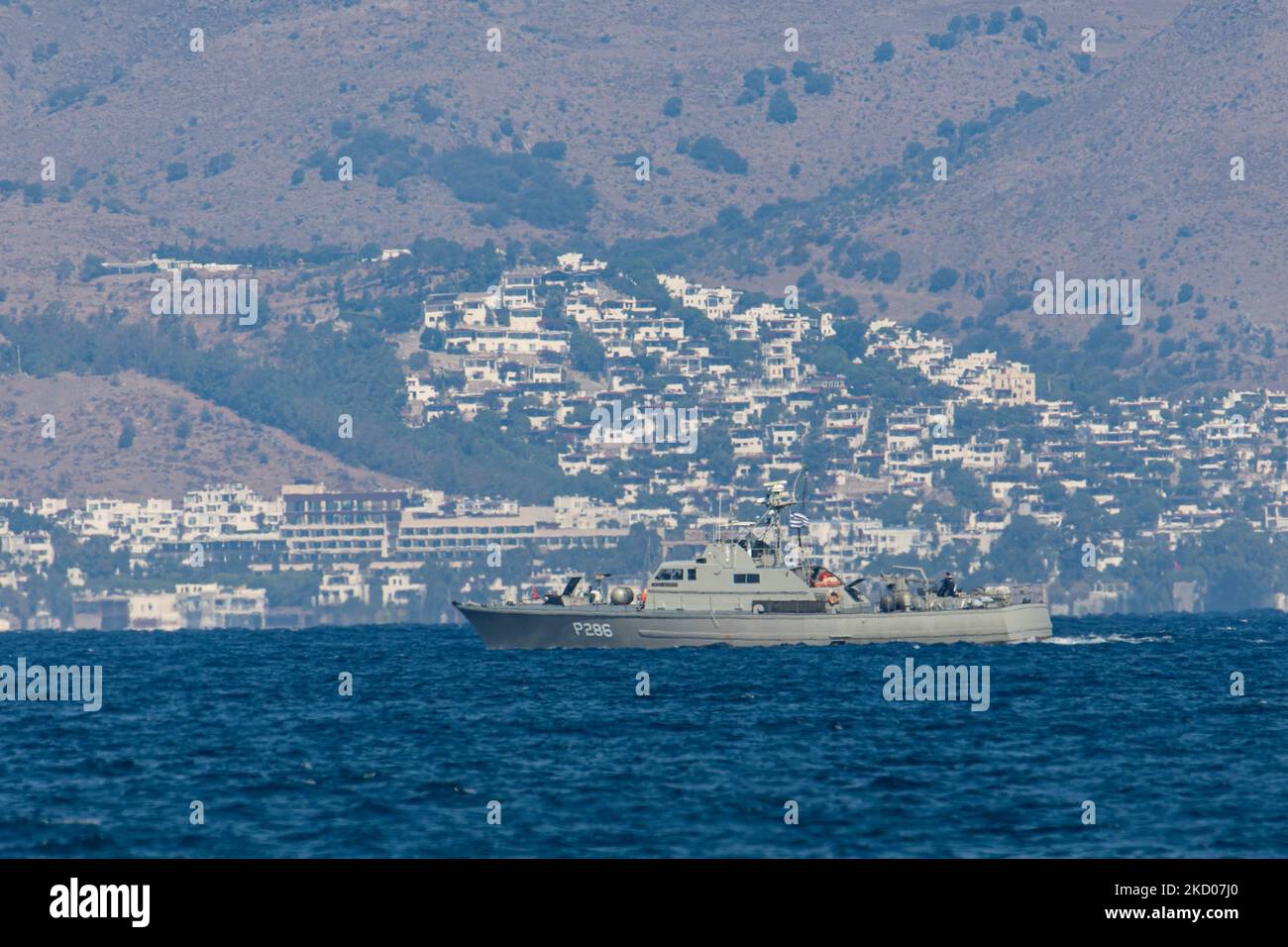 Una nave di pattuglia greca della Marina ellenica sta pattugliando i confini dell'acqua del Mar Egeo tra la Grecia e la Turchia, appena fuori dall'isola di Kos con la Turchia sullo sfondo con case estive, resort e alberghi visibili. I pattugliamenti sono destinati a scopi militari, ma anche a imbarcazioni con rifugiati e migranti, oltre alla forza FRONTEX che protegge i confini europei dalla crisi dei rifugiati. La nave che pattuglia i richiedenti asilo che cercano di attraversare con un gommone della costa turca è una piccola nave missilistica di classe Diopos Antoniou P286 Hellenic Navys Kelefstis Stamou. L'isola di Kos e la costa turca fr Foto Stock