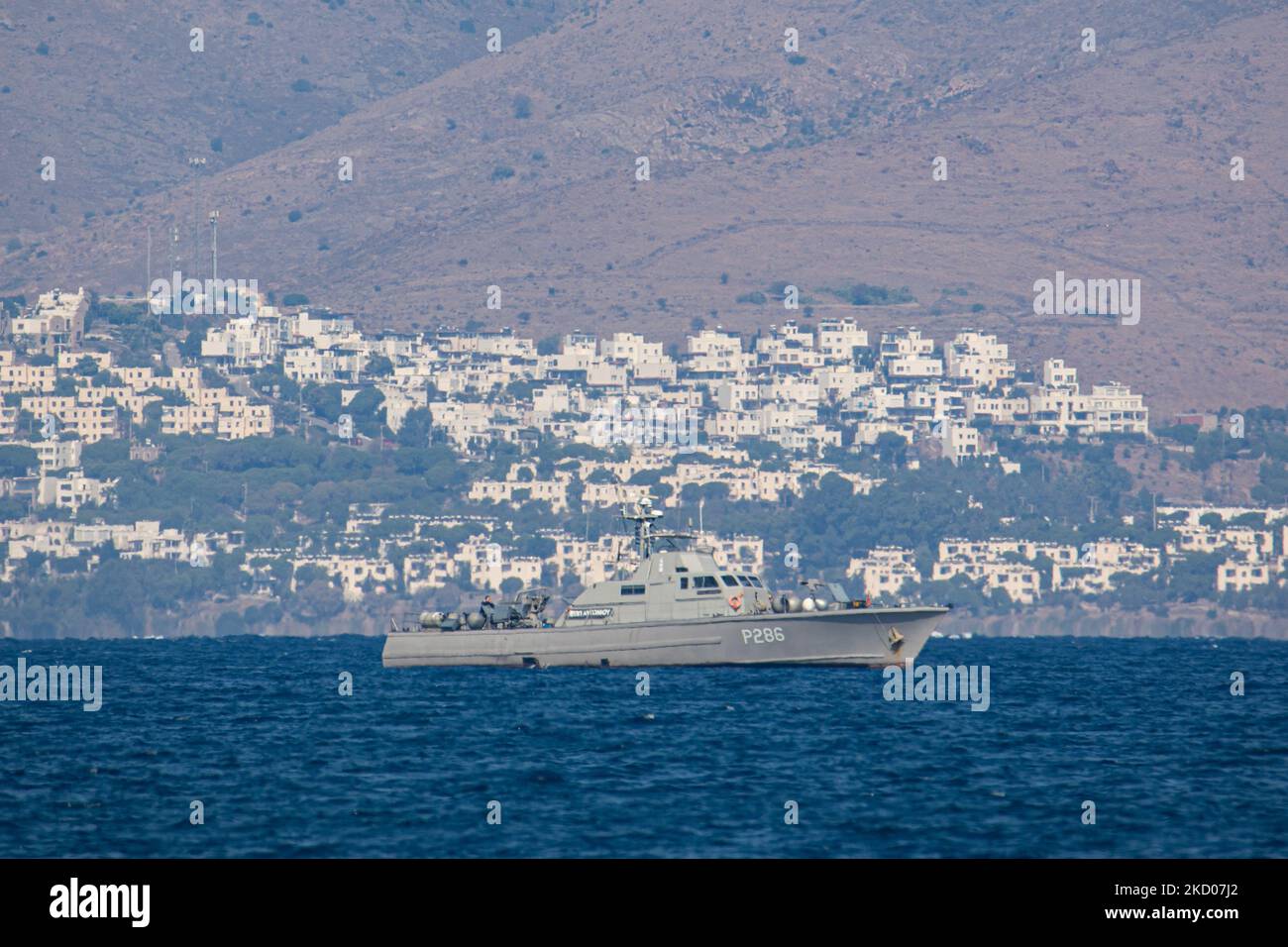 Una nave di pattuglia greca della Marina ellenica sta pattugliando i confini dell'acqua del Mar Egeo tra la Grecia e la Turchia, appena fuori dall'isola di Kos con la Turchia sullo sfondo con case estive, resort e alberghi visibili. I pattugliamenti sono destinati a scopi militari, ma anche a imbarcazioni con rifugiati e migranti, oltre alla forza FRONTEX che protegge i confini europei dalla crisi dei rifugiati. La nave che pattuglia i richiedenti asilo che cercano di attraversare con un gommone della costa turca è una piccola nave missilistica di classe Diopos Antoniou P286 Hellenic Navys Kelefstis Stamou. L'isola di Kos e la costa turca fr Foto Stock
