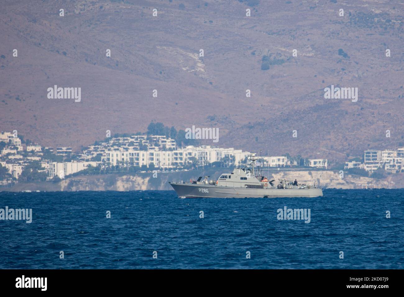Una nave di pattuglia greca della Marina ellenica sta pattugliando i confini dell'acqua del Mar Egeo tra la Grecia e la Turchia, appena fuori dall'isola di Kos con la Turchia sullo sfondo con case estive, resort e alberghi visibili. I pattugliamenti sono destinati a scopi militari, ma anche a imbarcazioni con rifugiati e migranti, oltre alla forza FRONTEX che protegge i confini europei dalla crisi dei rifugiati. La nave che pattuglia i richiedenti asilo che cercano di attraversare con un gommone della costa turca è una piccola nave missilistica di classe Diopos Antoniou P286 Hellenic Navys Kelefstis Stamou. L'isola di Kos e la costa turca fr Foto Stock