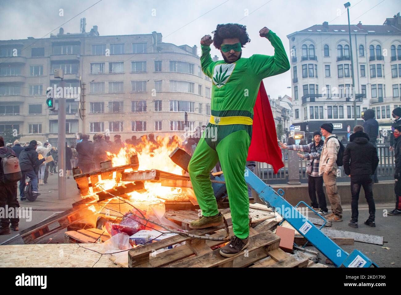 Un uomo in una suite sta posando sul blocco della strada barricata sul fuoco. Migliaia di persone protestano durante la dimostrazione europea per la democrazia contro le misure correlate a Covid come il pass sanitario COVID e le restrizioni. I disordini hanno cominciato a scoppiare e la polizia spara gas lacrimogeni e cannone d'acqua mentre la protesta si è trasformata in violenta. La gente partecipa a una manifestazione contro le misure sanitarie a Bruxelles come il COVID Health Pass, il codice QR, le maschere facciali e la vaccinazione obbligatoria, usando come slogan principale e sulle bandiere il termine liberte tradotto come libertà. Le autorità stimano che circa 50.000 persone provenienti da tutto il paese Foto Stock