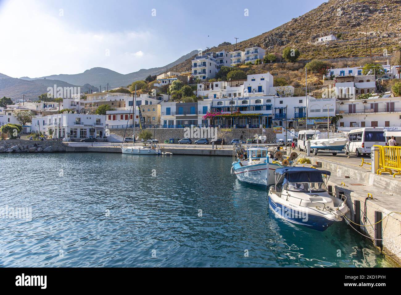 Scena del porto dell'isola con alcune piccole barche ormeggiate. Livadia, il porto e il villaggio principale dell'isola di Tilos con le case di architettura tradizionale imbiancate e la spiaggia con le acque cristalline del mare. Telos è una piccola isola greca mediterranea nel Mar Egeo, parte delle isole Dodecanesi, con una popolazione di 780 abitanti vicino alla costa turca. Alla fine del 2018 Tilos è diventata la prima isola del Mediterraneo a funzionare esclusivamente con energia eolica e solare, un'isola verde autosufficiente, un'iniziativa finanziata dall'UE per l'energia verde da fonti rinnovabili che proteggono il natu Foto Stock