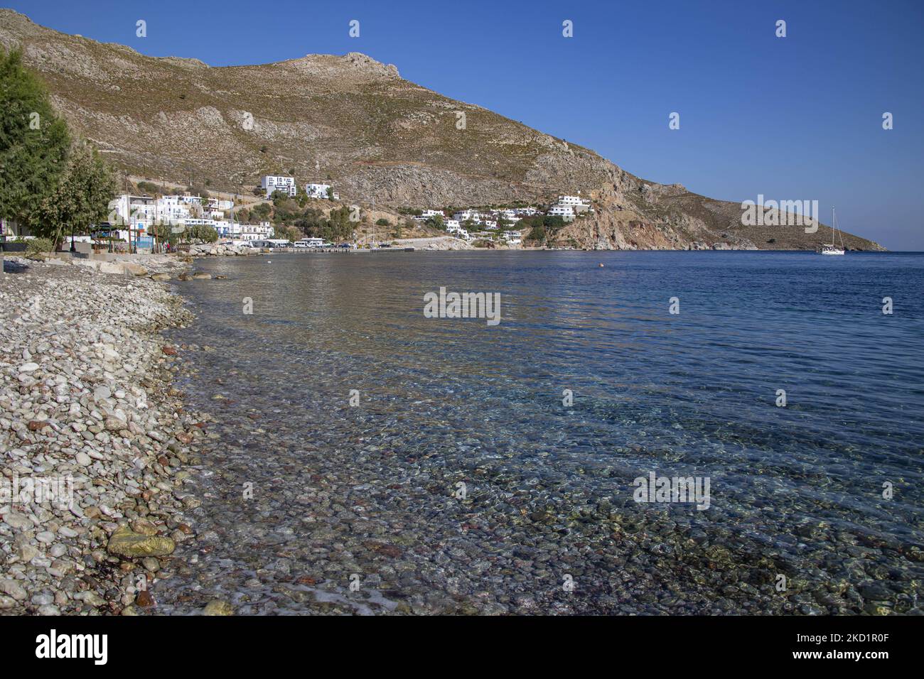 La spiaggia di ciottoli di Livadia. Livadia, il porto e il villaggio principale dell'isola di Tilos con le case di architettura tradizionale imbiancate e la spiaggia con le acque cristalline del mare. Telos è una piccola isola greca mediterranea nel Mar Egeo, parte delle isole Dodecanesi, con una popolazione di 780 abitanti vicino alla costa turca. Alla fine del 2018 Tilos è diventata la prima isola del Mediterraneo a funzionare esclusivamente con energia eolica e solare, un'isola verde autosufficiente, un'iniziativa finanziata dall'UE per l'energia verde da fonti rinnovabili a tutela dell'ambiente naturale. Isola di Tilos, Cree Foto Stock
