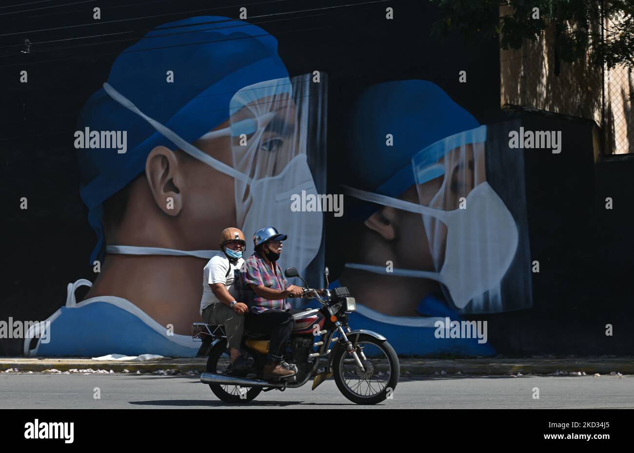 I motociclisti che indossano una maschera facciale passano davanti a un murale di un operaio essenziale dipinto nel centro di Merida dagli artisti messicani Mare - Noookye. Sabato 19 febbraio 2022 a Merida, Yucatan, Messico. (Foto di Artur Widak/NurPhoto) Foto Stock