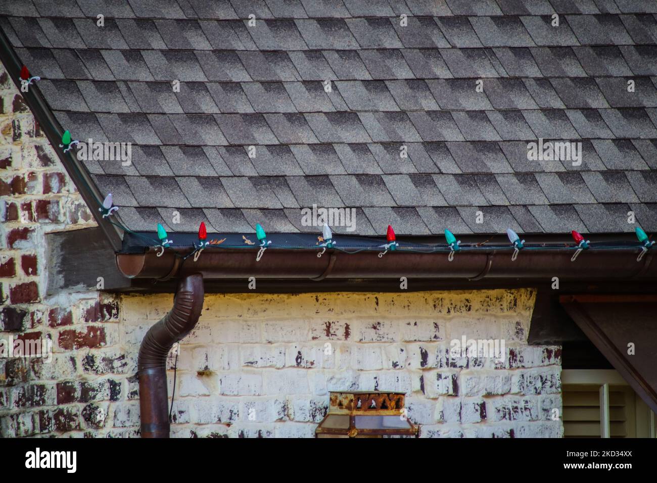 Primo piano di rame grondaia di casa di mattoni con schermo e montato rosso e verde luci di decorazione Natale Foto Stock