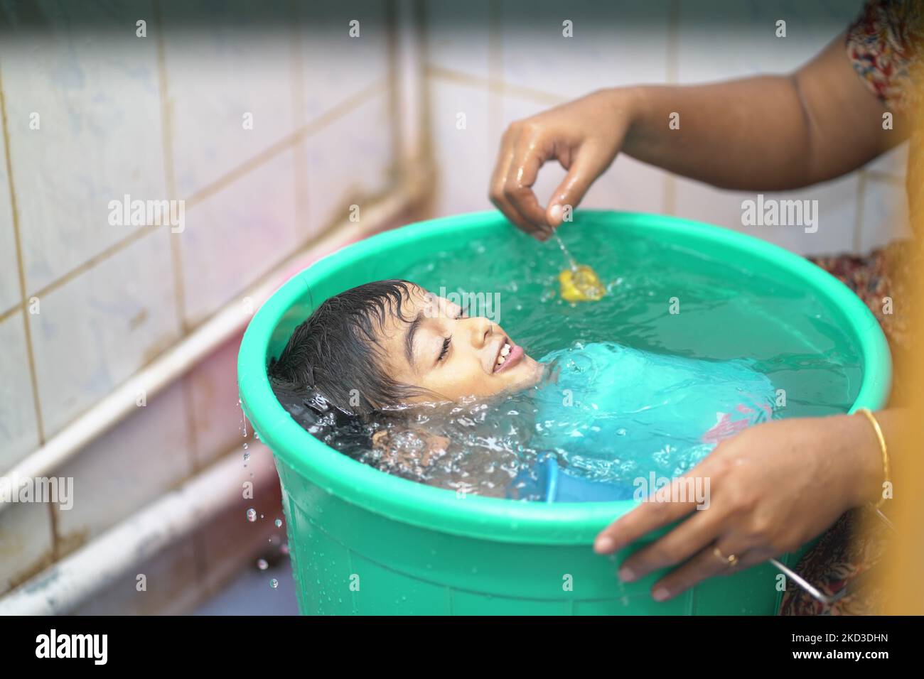 La madre lava il suo piccolo ragazzo indiano in un grande secchio Foto Stock