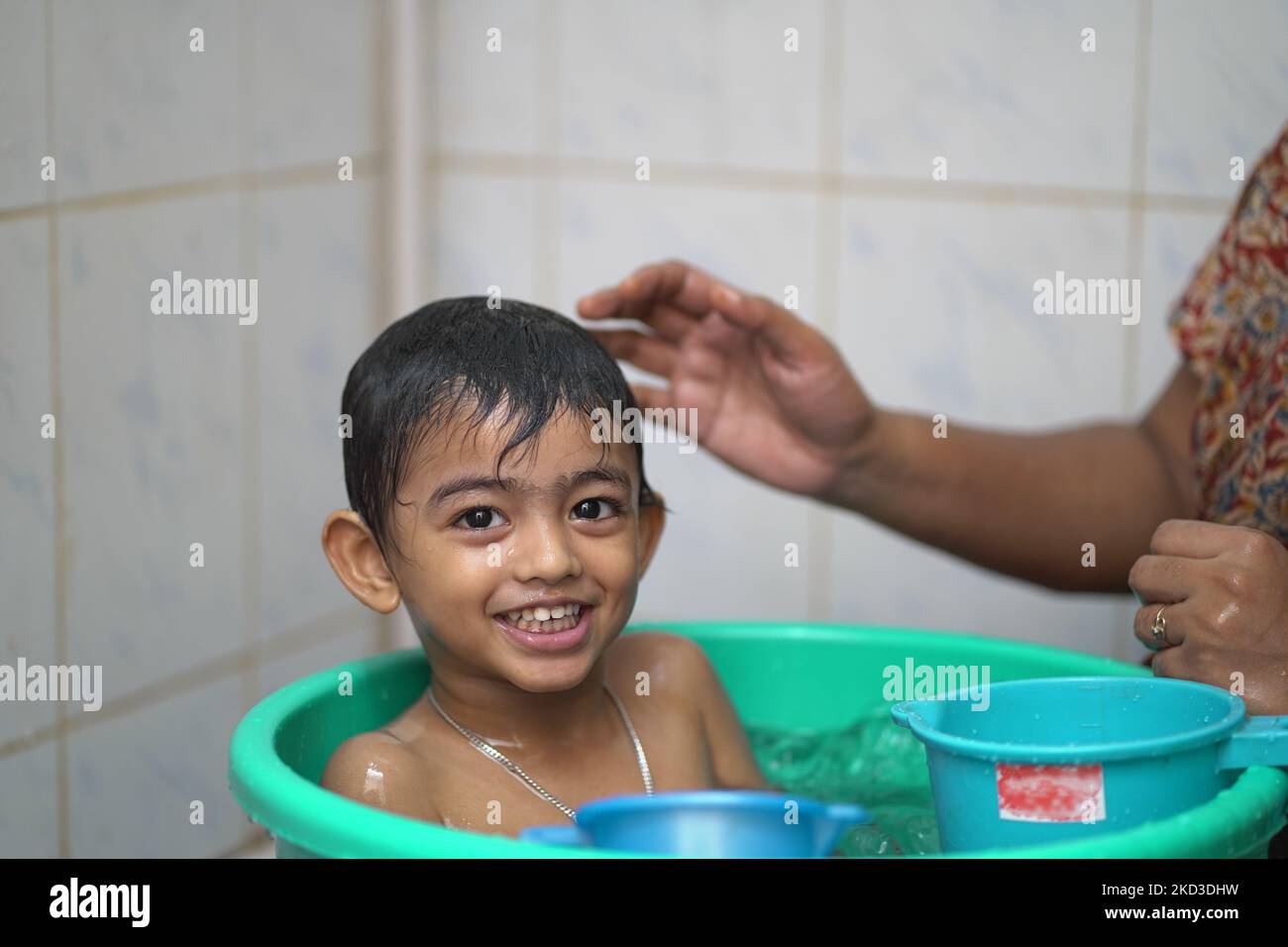La madre lava il suo piccolo ragazzo indiano in un grande secchio Foto Stock