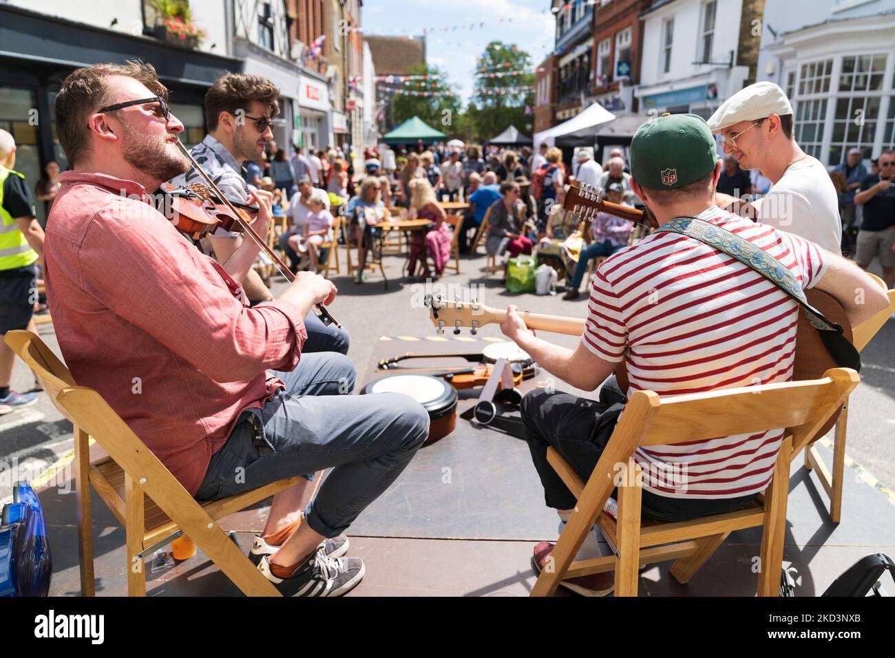 Vista a spalla di quattro giocatori folcloristici seduti su un piccolo palco di fronte a un pubblico nella strada principale della città medievale di Sandwich nel Kent Foto Stock
