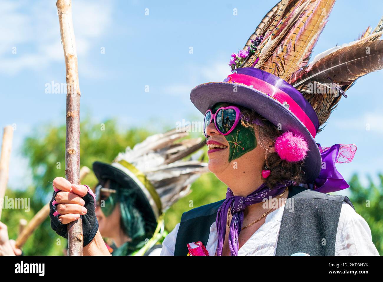 Primo piano del volto della danzatrice Morris con il volto dipinto di verde e il cappello in piuma mentre ballate in un evento all'aperto. Foto Stock