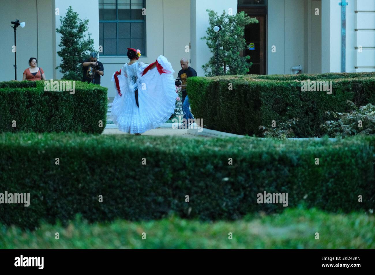Una parte posteriore di una donna che indossa un costume regionale messicano e la tiene in su con fiducia, passanti intorno, in un parco verde della macchia Foto Stock