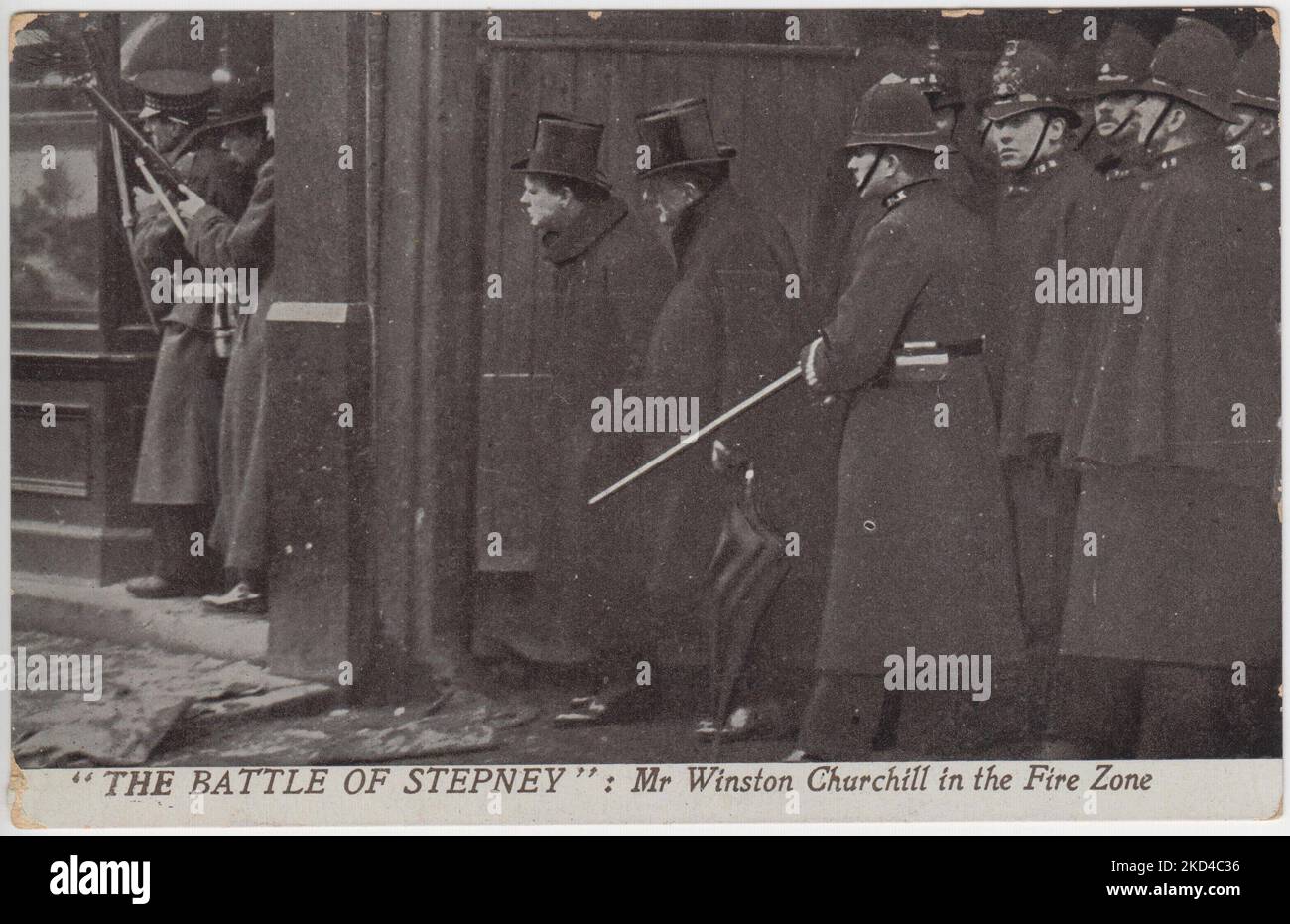 "La battaglia di Stepney: Winston Churchill nella zona dei vigili del fuoco": Cartolina dell'assedio di Sidney Street del 1911, con il segretario generale Winston Churchill che sbirciava lungo Sidney Street nella casa assediata, indossando un cappello. Soldati con fucili sono in piedi davanti a lui e un gruppo di poliziotti sono dietro di lui. Foto Stock