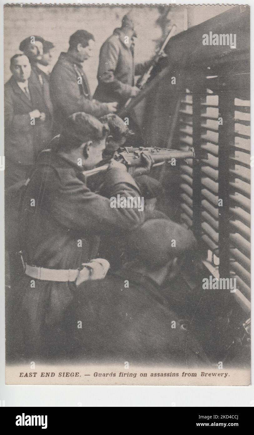 'East End Assedio. - Guardie che sparano contro assassini da Brewery': Cartolina dell'assedio del 1911 di Sidney Street, che mostra soldati armati di fucili che si preparano a sparare agli occupanti di 100 Sidney Street attraverso finestre chiuse Foto Stock