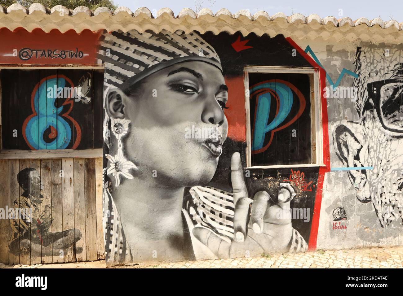 Street Art. Un murale di una donna africana e di un ragazzo seduto a croce zampe dipinte su un vecchio edificio. Lagos, Algarve, Portogallo Foto Stock
