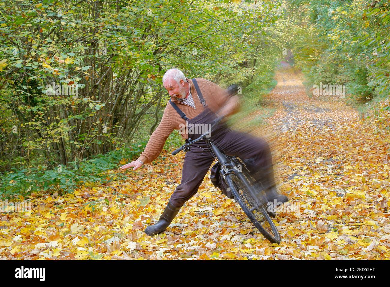 Il ciclista anziano si schianta sulla pista ciclabile coperta di foglie. Foto Stock