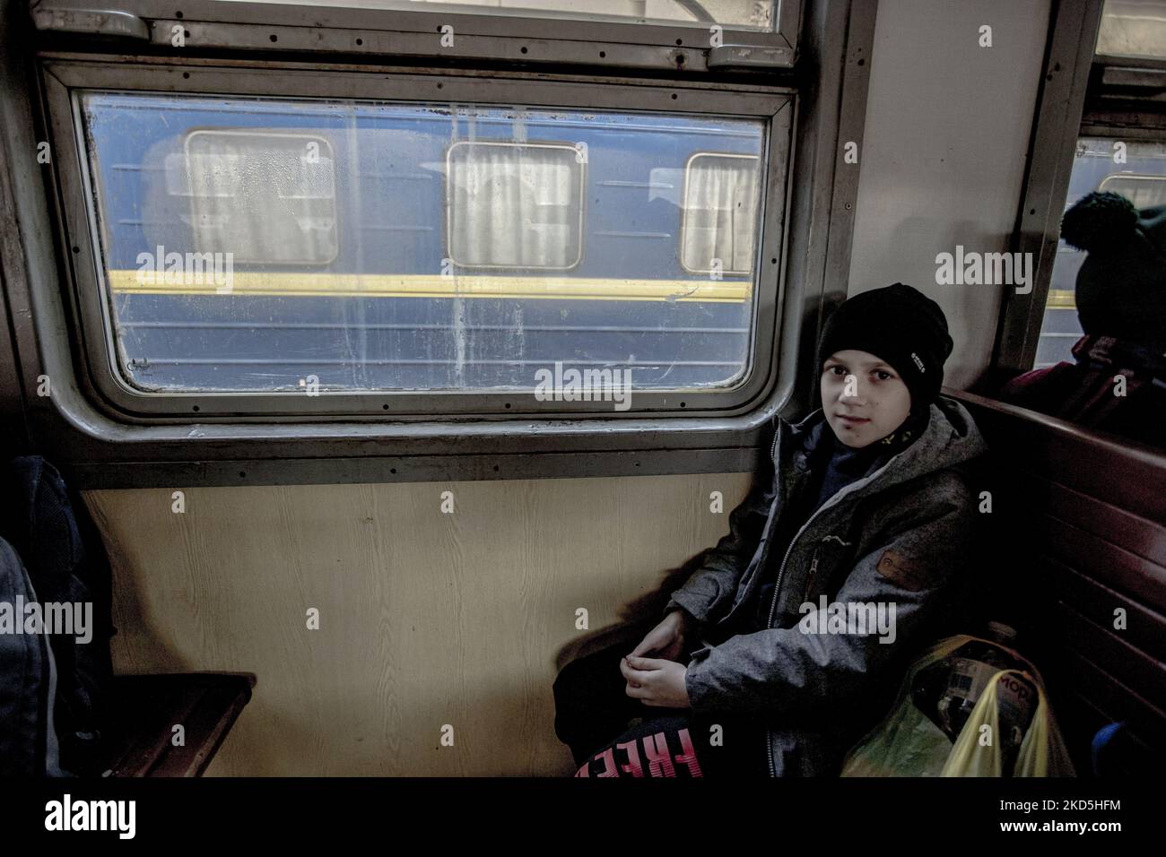 Un ragazzo seduto da solo in treno. La gente Ucraina in una vecchia macchina ferroviaria arrivare velocemente dopo l'attesa metropolitana a Lviv stazione ferroviaria passaggio il treno per arrivare e salire a bordo delle carrozze perché la stazione è considerata come un obiettivo militare. Il treno attraverserà le frontiere ucraine polacche e si sposterà ulteriormente verso la Polonia e altri paesi europei. Il 15 marzo le sirene per RAID aereo suonavano due volte, una al mattino e una alla sera. Secondo le Nazioni Unite - UNHCR più di 3,3 milioni di rifugiati hanno lasciato il paese come annunciato dalle Nazioni Unite e hanno mostrato i dati su una mappa mentre a. Foto Stock