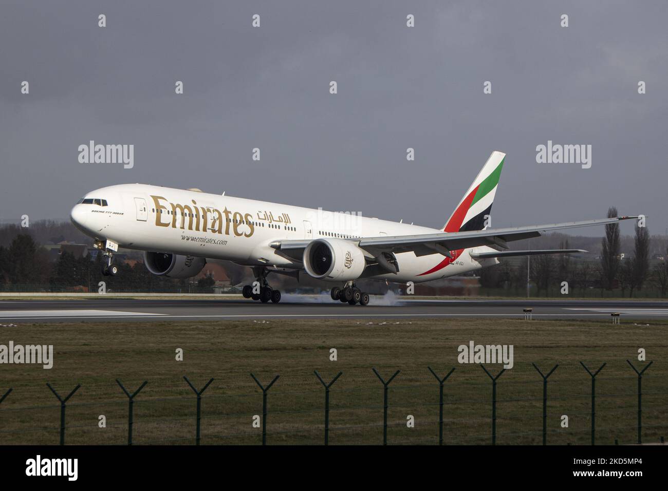 Emirates Boeing 777 come visto volare e atterrare sulla pista con la torre di controllo e le nuvole sullo sfondo. Emirates B777 come visto all'avvicinamento finale in volo, atterraggio e tassazione presso la capitale belga, l'aeroporto Zaventem BRU di Bruxelles. Il Boeing Boeing 777-31HER moderno e avanzato velivolo passeggeri a fusoliera larga ha la registrazione A6-EQJ ed è alimentato da motori a reazione 2x GE90. L'aereo arriva alla città europea da Dubai DXB, Emirati Arabi Uniti. Emirates è la più grande compagnia aerea e una delle due compagnie di bandiera degli Emirati Arabi Uniti. L'industria aeronautica e il traffico passeggeri Foto Stock