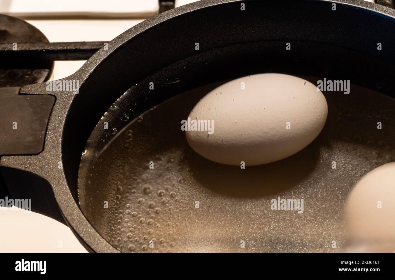 Uovo di pollo bianco primo piano con bolle d'acqua bollente in pentola nera su stufa a gas Foto Stock